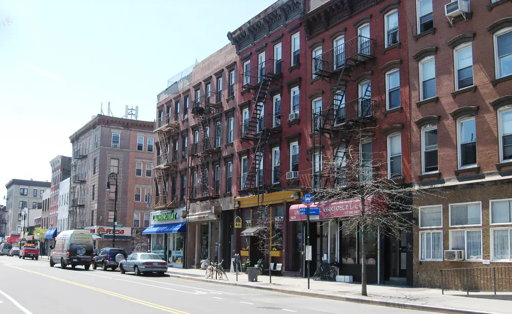 A Greenpoint, Brooklyn street corner with low brick buildings, shopfronts and parked cars under a clear sky