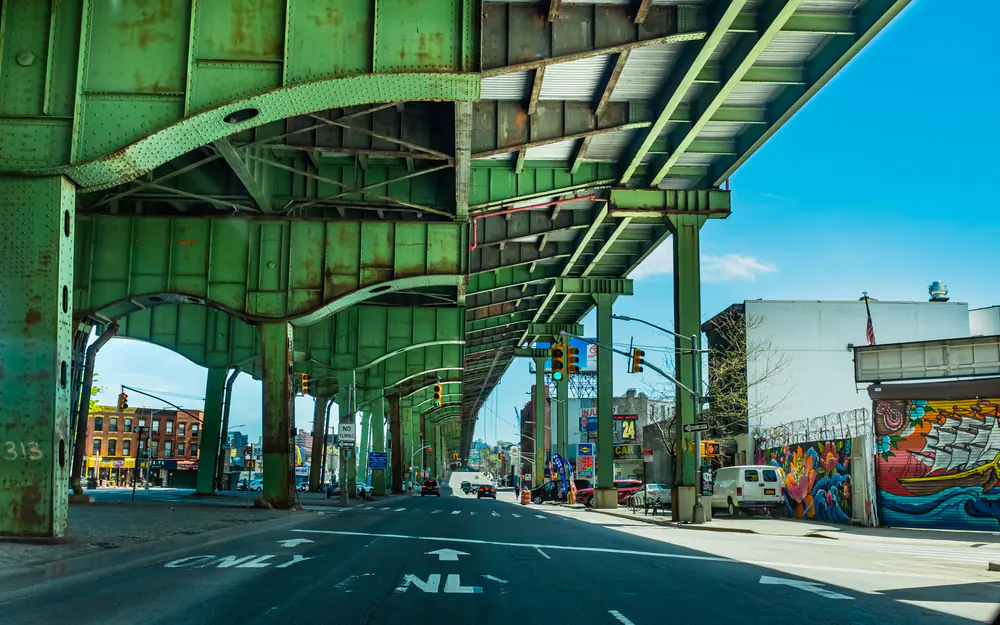 Hamilton Avenue in Brooklyn running beneath the green steel underside of the Gowanus Expressway, with a mural on the right
