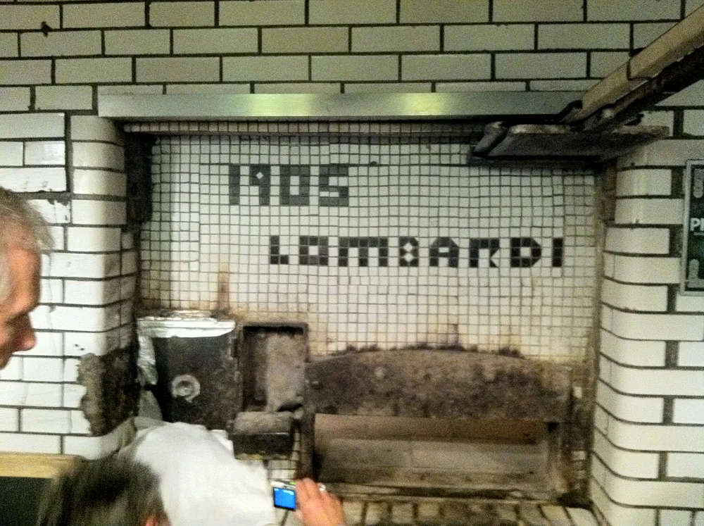 The white-tiled front of Lombardi's coal oven, 1905 and LOMBARDI spelled in dark tile above the closed door