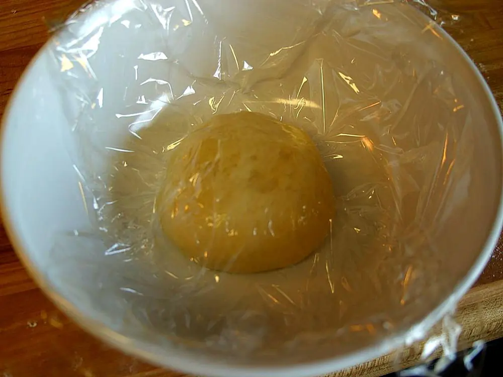 A pair of hands pressing and stretching a round of pale pizza dough on a floured wooden surface