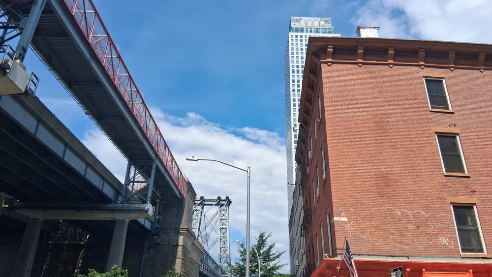 The red steel viaduct of the Williamsburg Bridge passing a nineteenth-century brick warehouse